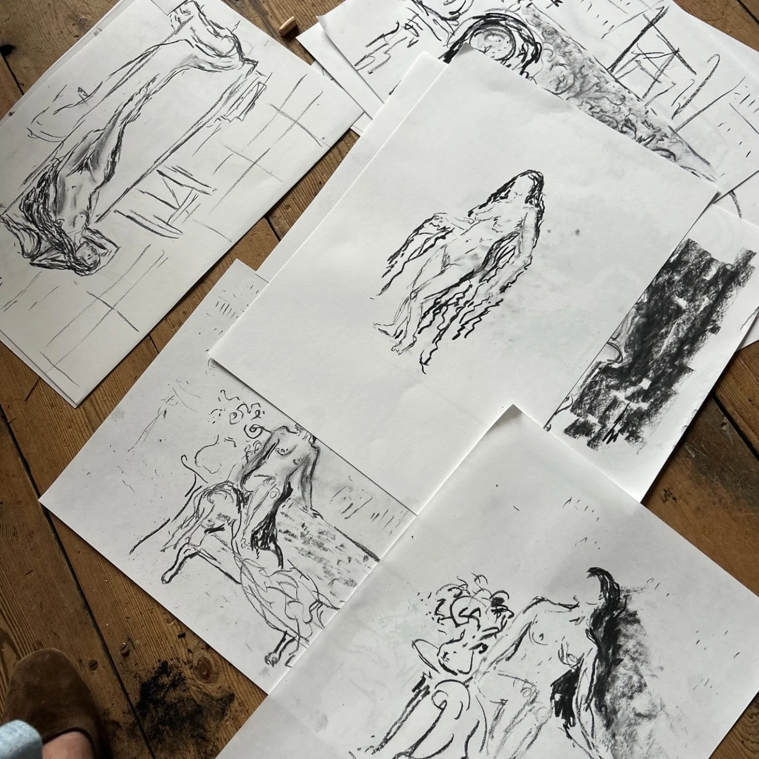 Charcoal figure studies arranged across a wooden floor