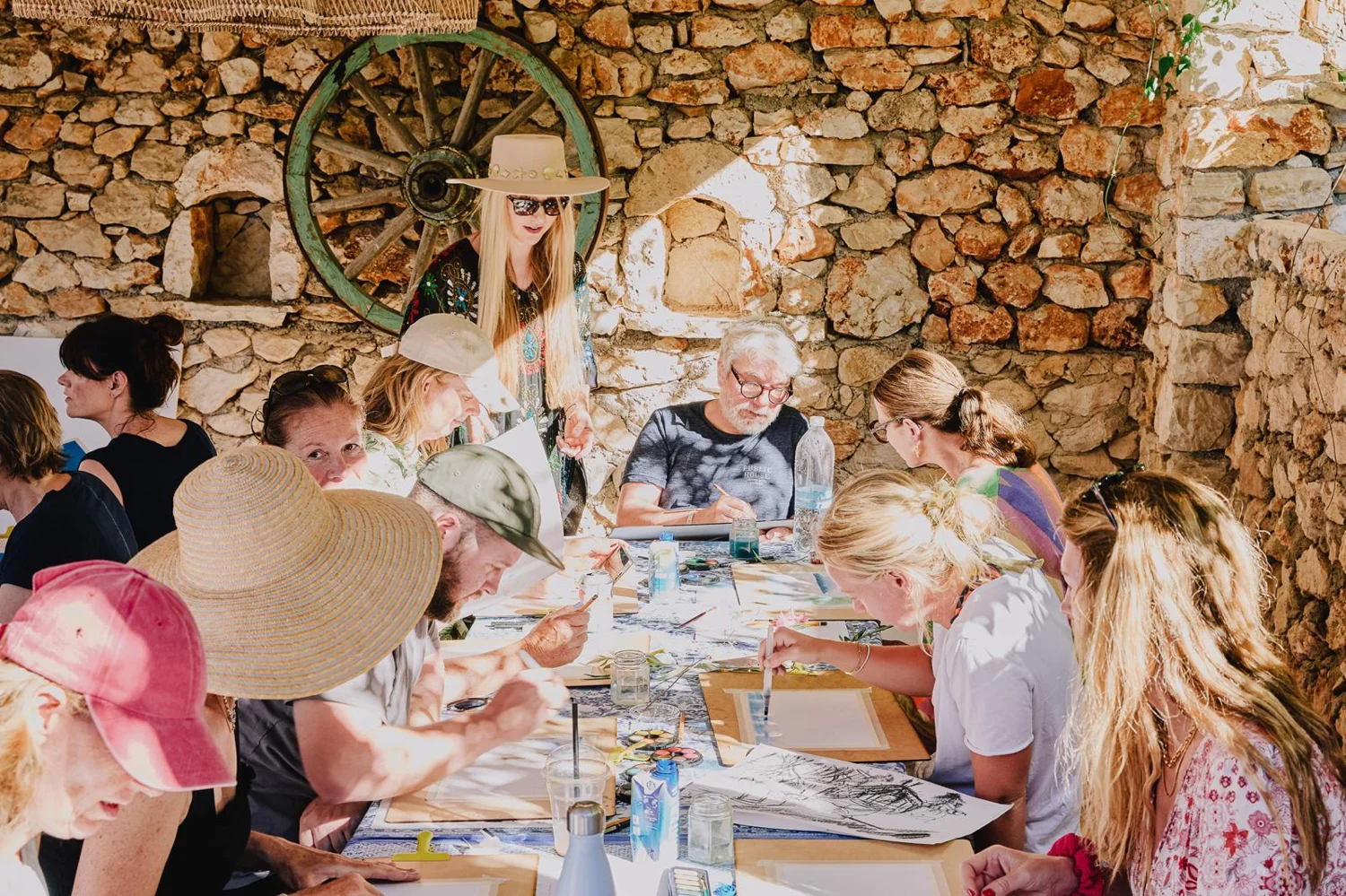 A group drawing together beside a stone wall on a painting holiday